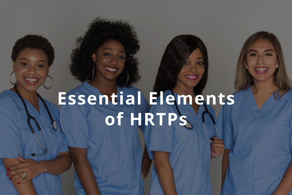 Four multiethnic women wearing blue scrubs smiling at the camera.