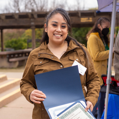 Hispanic woman smiling at the camera holding a completion certificate.