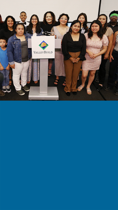 Group of multicultural females next to a podium with Valley Build logo smiling at the camera.